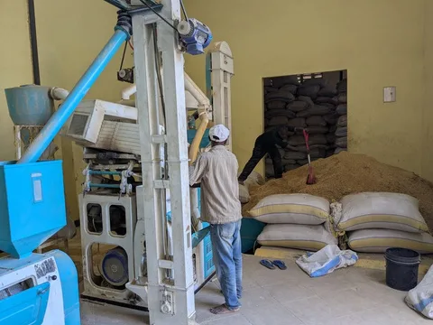 Operator running the rice milling plant at Mlandizi beside stacked paddy sacks